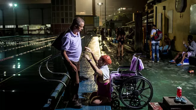 Nadadora discapacitada con los brazos arriba, esperando que su entrenador la ayude a subirse a su silla de ruedas