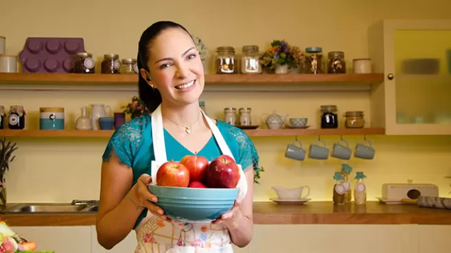 Paulina Abascal en la cocina, sosteniendo una taza llena de manzanas