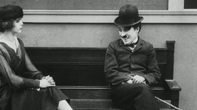 Charles Chaplin sentado en una banca sonriéndole a una mujer