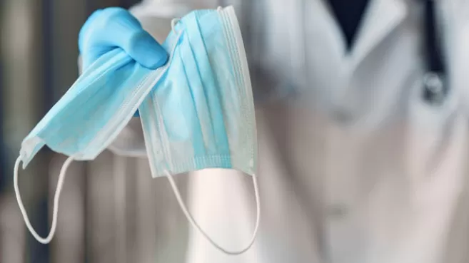 Doctor sostiene dos tapabocas quirurgicos azules en su mano