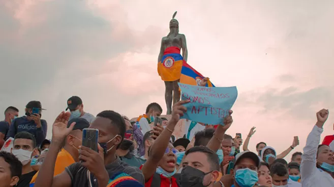 India Catalina vestida con la bandera de Colombia al revés, rodeada de manifestantes pacíficos