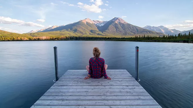Mujer de espaldas sentada en un muelle contemplando un lago y las montañas