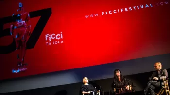 Dos mujeres y un hombre sentados junto a un anuncio rojo del FICCI