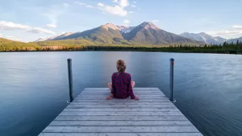 Mujer de espaldas sentada en un muelle contemplando un lago y las montañas