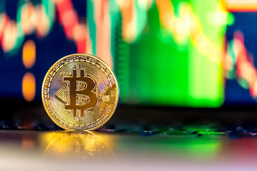 Moneda de Bitcoin sobre un teclado de laptop con la gráfica de velas japonesas en la pantalla