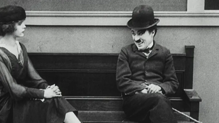 Charles Chaplin sentado en una banca sonriéndole a una mujer