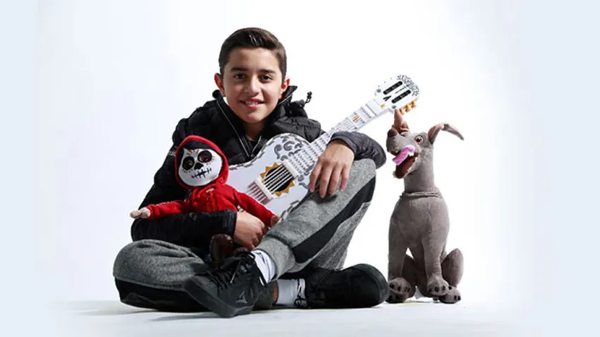 Luis Ángel Gómez Jaramillo sentado en el piso con una guitarra y dos peluches de la película Coco