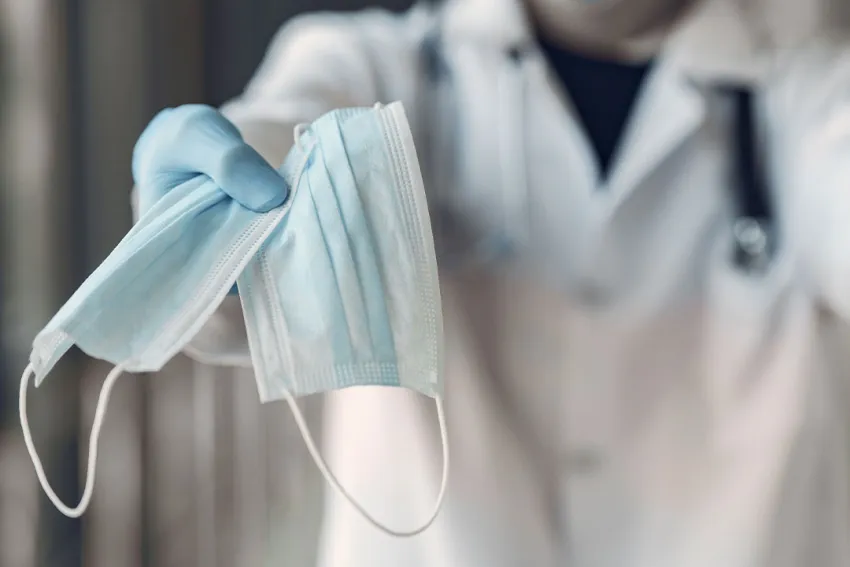 Doctor sostiene dos tapabocas quirurgicos azules en su mano