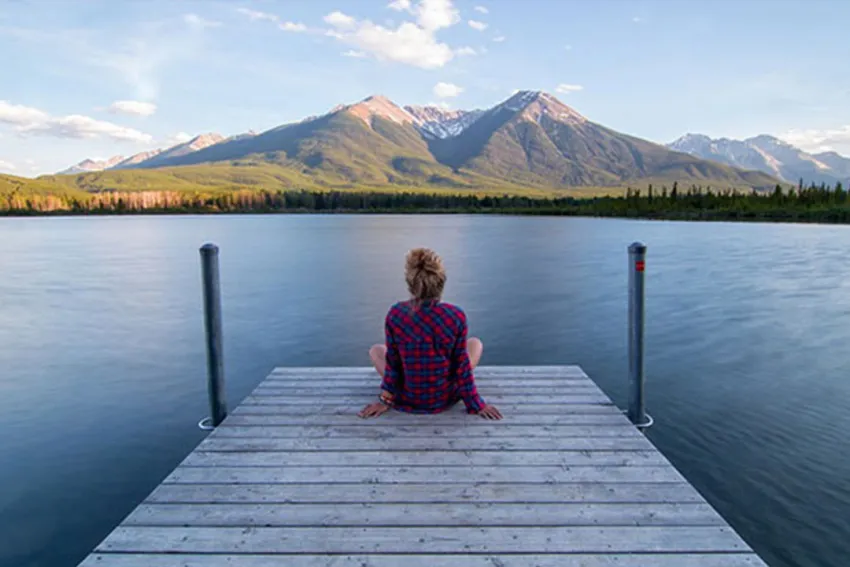 Mujer de espaldas sentada en un muelle contemplando un lago y las montañas