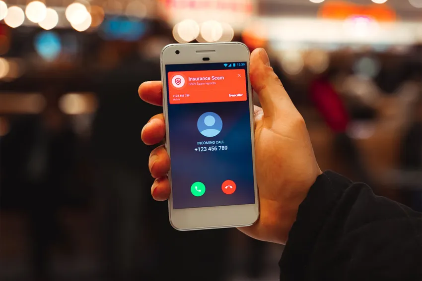 Mano de hombre sosteniendo un celular que muestra en pantalla una llamada spam