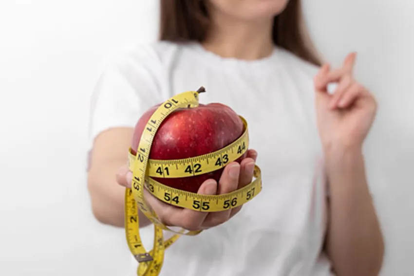 Mujer sostiene una manzana roja envuelta en una cinta métrica