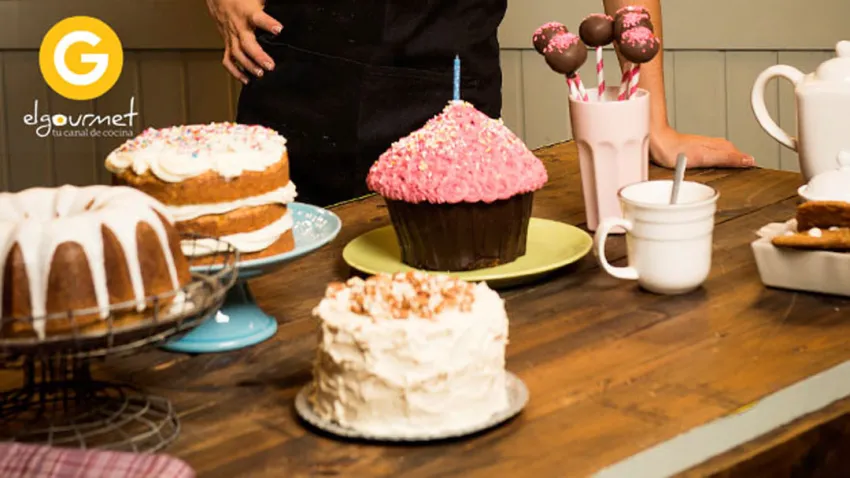 Varias tortas y bombones en una mesa, al fondo se ven las manos de la chef Alma Obregón