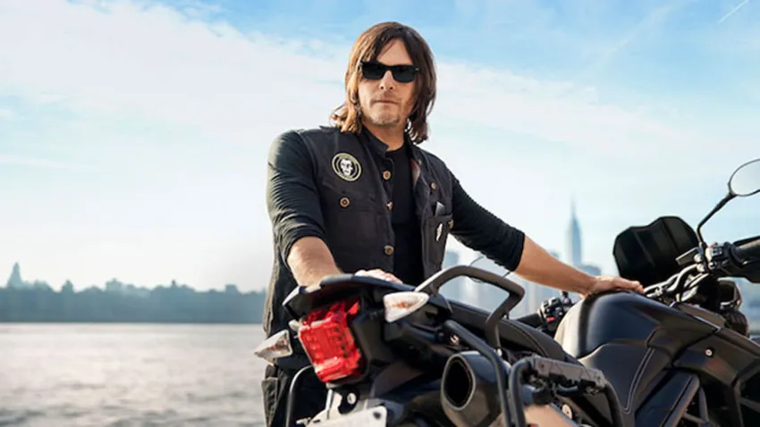 Norman Reedus vestido de negro parado al lado de su motocicleta