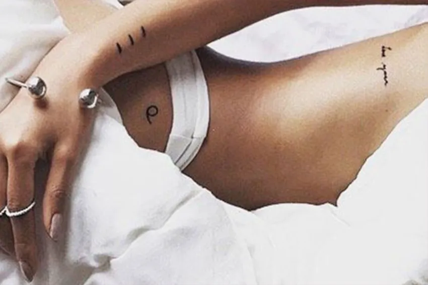 Mujer entre sábanas blancas mostrando tatuajes de su cadera, costado y brazo derecho