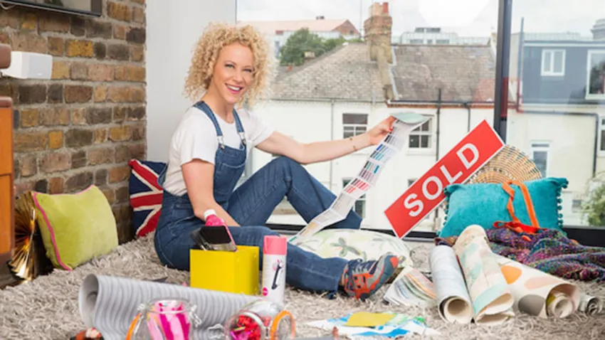 Tracy Metro sentada en una alfombra con materiales de remodelación y un letrero que dice "SOLD"