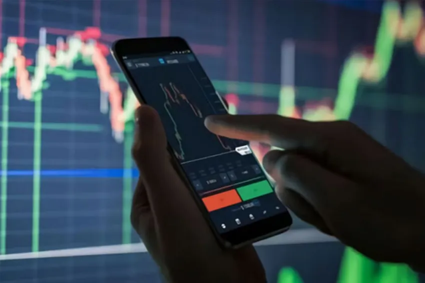 Manos haciendo trading desde el móvil y de fondo el gráfico del mercado