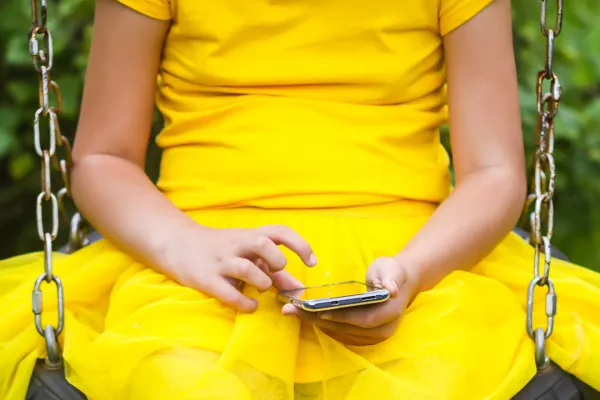 Niña usando un smartphone sentada en un columpio