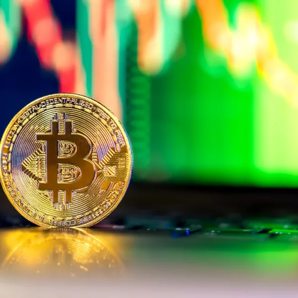 Moneda de Bitcoin sobre un teclado de laptop con la gráfica de velas japonesas en la pantalla