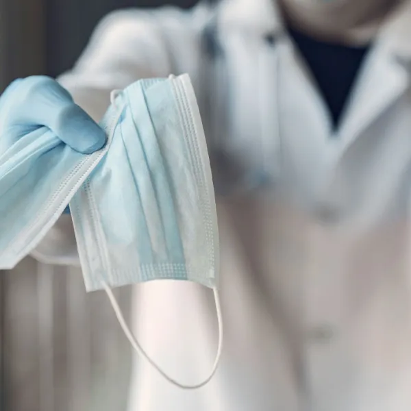 Doctor sostiene dos tapabocas quirurgicos azules en su mano