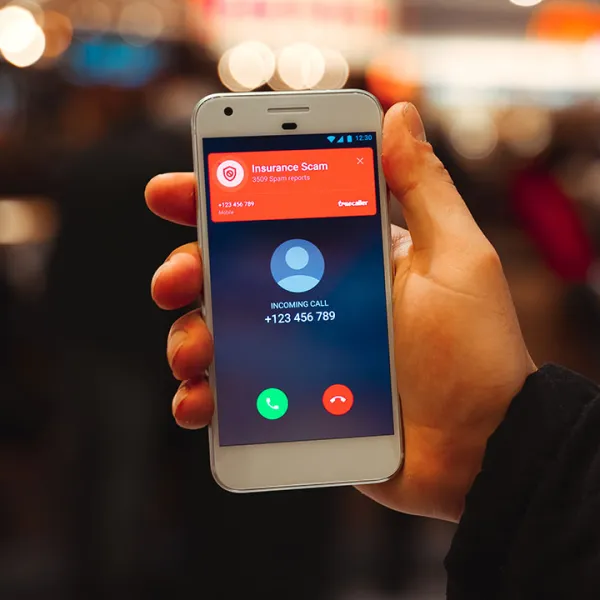 Mano de hombre sosteniendo un celular que muestra en pantalla una llamada spam