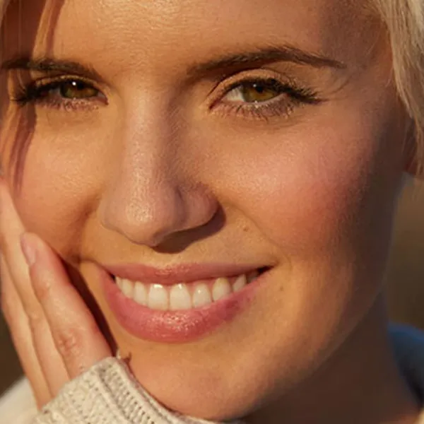 Maggie Grace en primer plano sonriendo y tocándose la cara