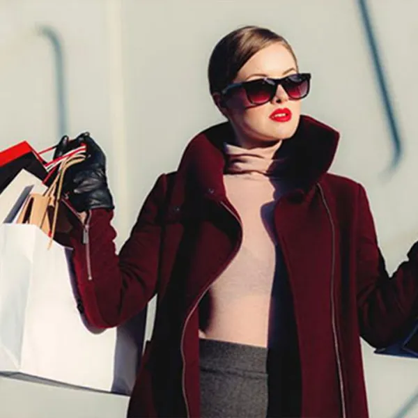 Mujer elegante con saco color vino tinto y gafas oscuras, cargando varias bolsas de compras en ambas manos