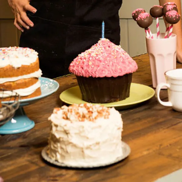 Varias tortas y bombones en una mesa, al fondo se ven las manos de la chef Alma Obregón