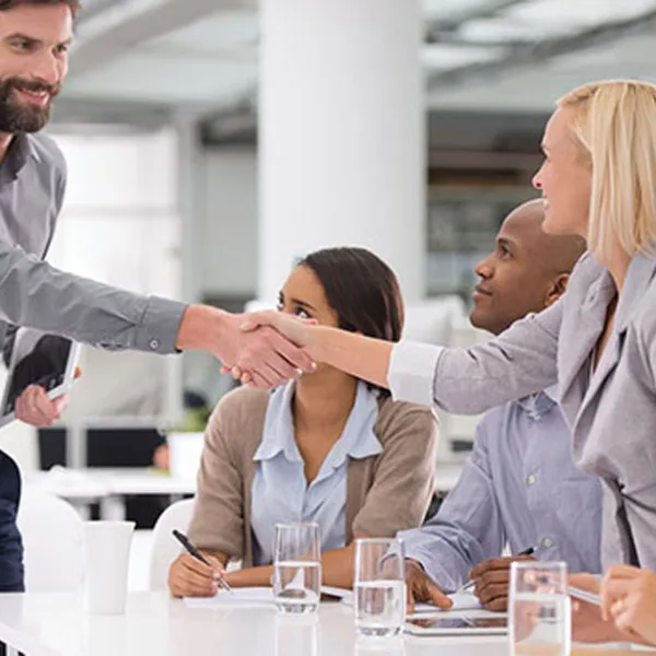 Hombre haciendo negocios con un grupo de personas en una oficina, le da la mano a una mujer