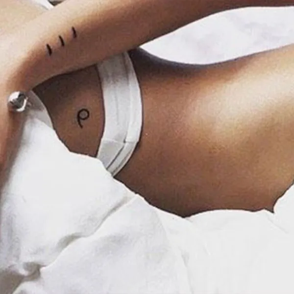 Mujer entre sábanas blancas mostrando tatuajes de su cadera, costado y brazo derecho