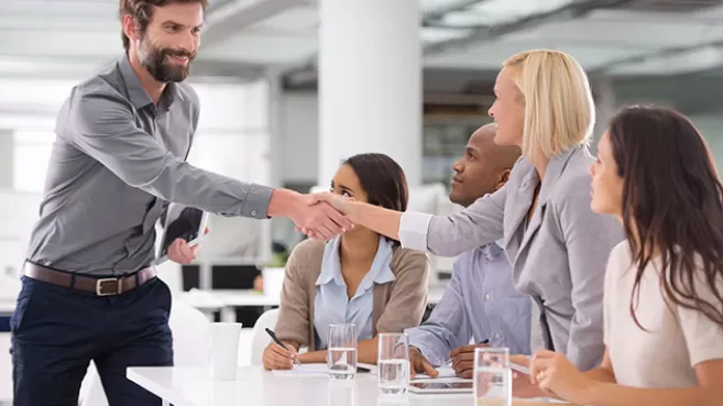 Hombre haciendo negocios con un grupo de personas en una oficina, le da la mano a una mujer