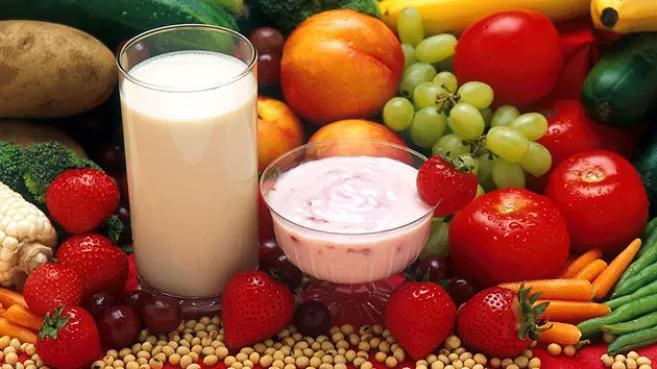 Vaso de leche y taza de yogurt rodeados de frutas y verduras