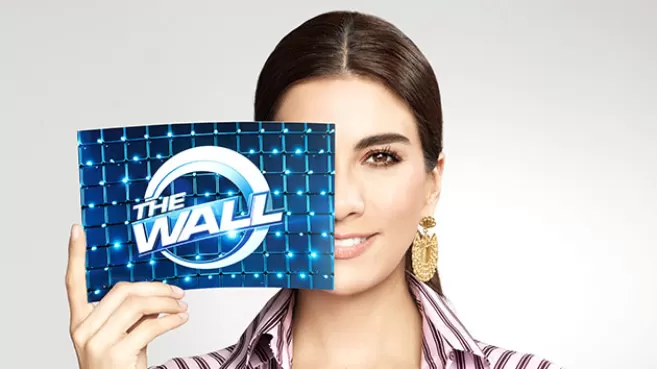 Andrea Serna tapándose media cara con una postal que tiene el logo de "The Wall"
