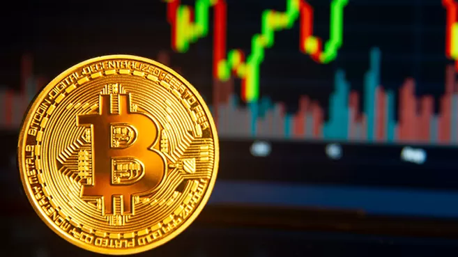 Una moneda dorada con el logo de Bitcoin, con su gráfica de fondo.